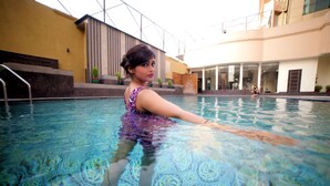 A swimming pool with a patterned floor, surrounded by a building with large windows and a yellow wall.