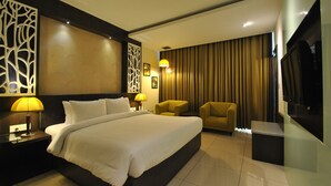 A modern hotel room with a large bed, two armchairs, a TV, and a decorative wall panel. - Rivatas (Varanasi)