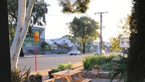 A wooden bench outside a building with a paved walkway, a statue, and a road with cars in the background. - Hello Adelaide Motel and Apartments (Frewville)