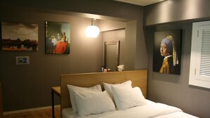 Una camera d'albergo con un letto, un comodino, uno specchio fissato alla parete e opere d'arte alle pareti.