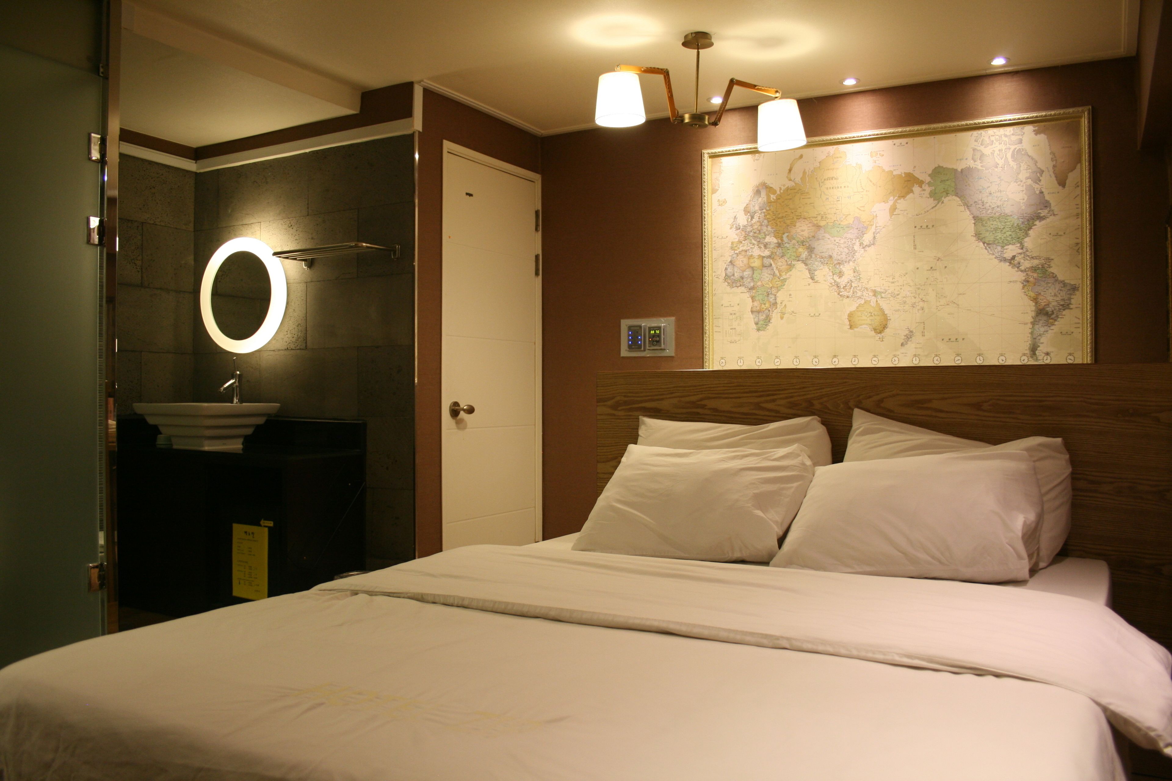 Quarto de hotel com cama, banheiro com pia e espelho, e um mapa-múndi na parede.