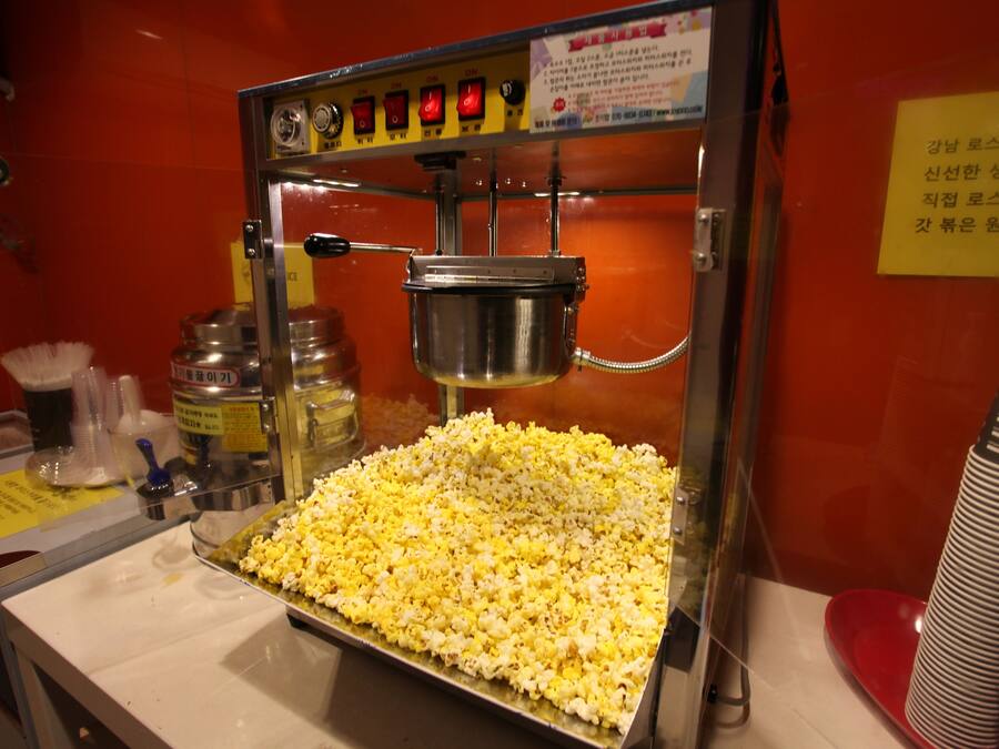 En popcornmaskin med en bricka full med popcorn och en metallbehållare ovanför.