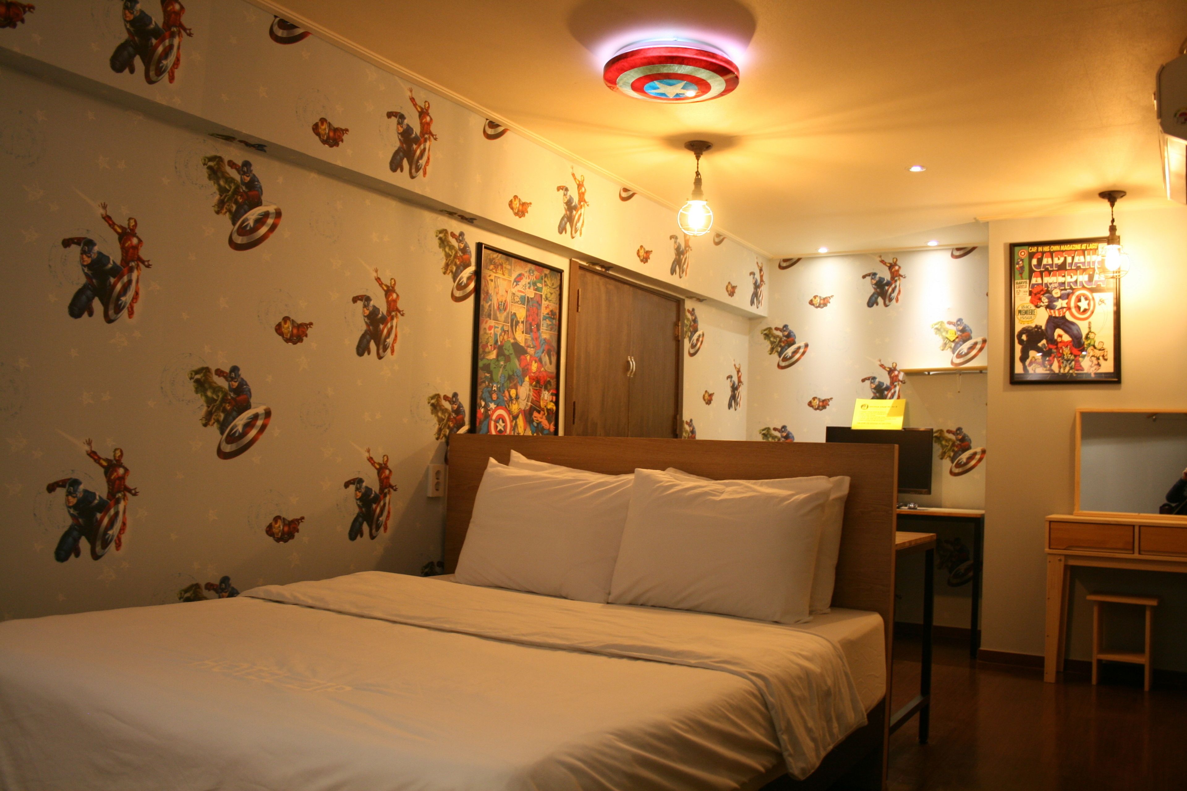 A bedroom with a bed, a desk, and a wall with superhero-themed decals.