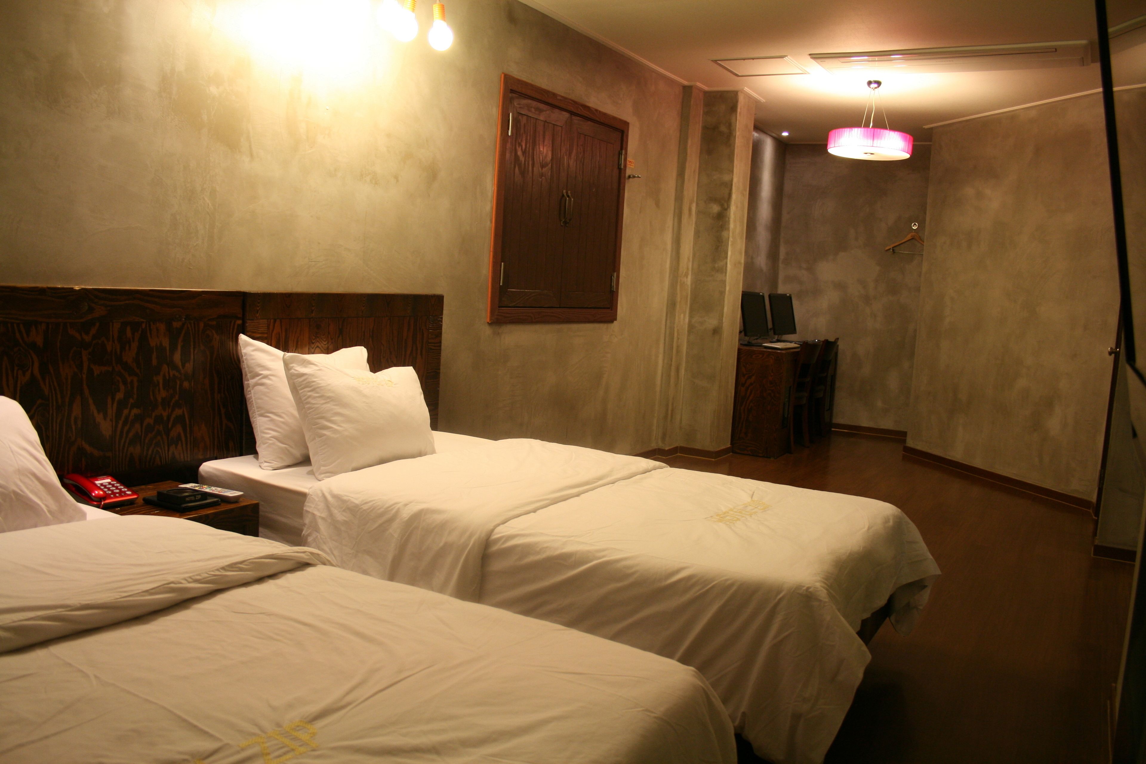 A hotel room with two beds, a wooden headboard, a nightstand, a telephone, and a hanging light fixture.