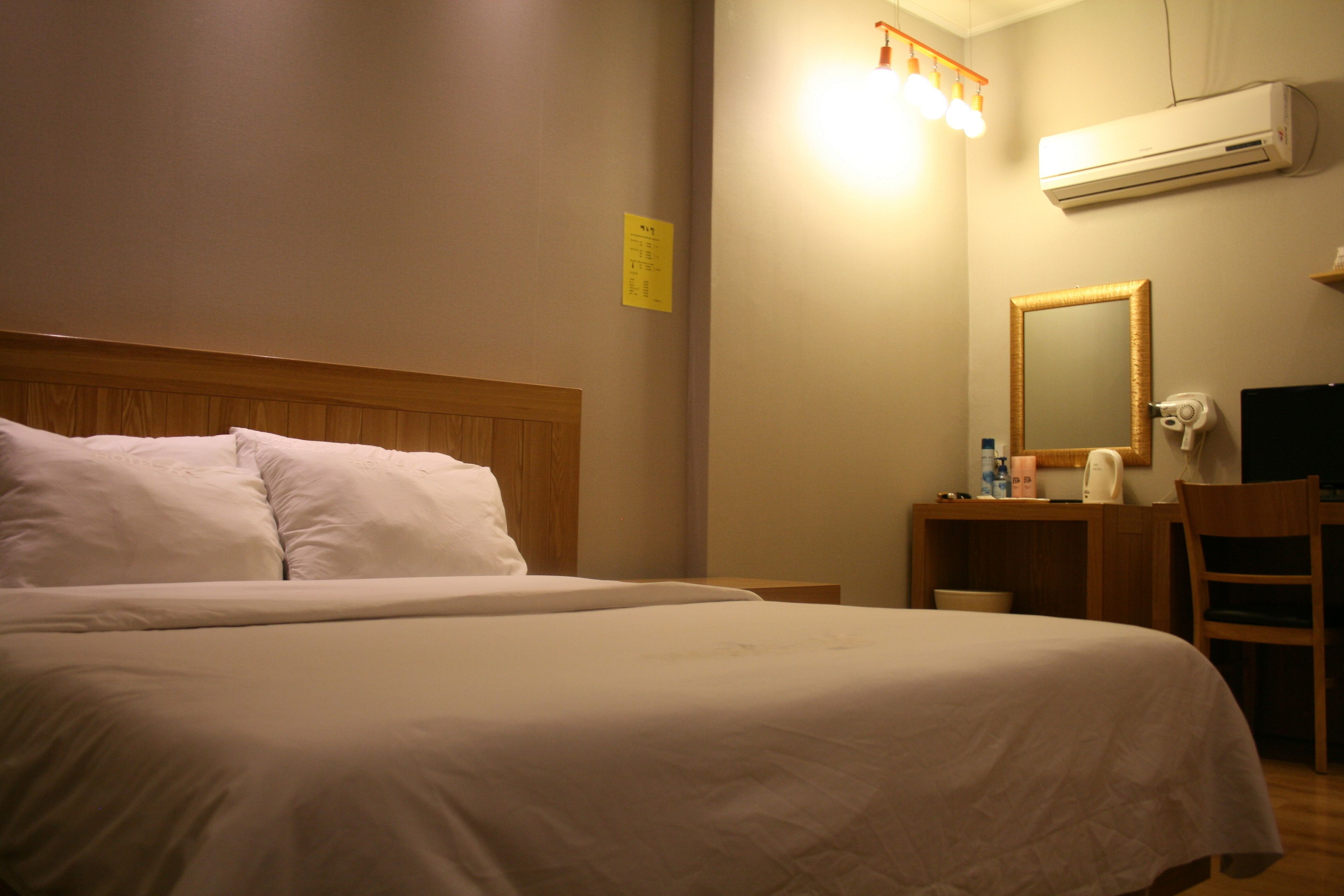 Ein Hotelzimmer mit einem großen Bett, einem hölzernen Kopfteil, einem Schreibtisch mit Stuhl, einem Spiegel und einer Klimaanlage.
