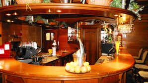 Un espace bar doté d’un comptoir en bois aux lignes courbes, d’une machine à café et d’un assortiment de bouteilles et de verres.