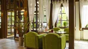 Un hall d’hôtel avec un canapé vert, une plante en pot et une vue sur l’extérieur grâce à de grandes fenêtres.