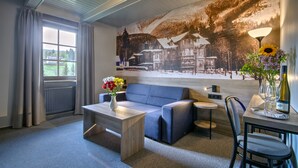 Un salon moderne avec un canapé bleu, une table basse en bois, une petite table ronde et un fauteuil. Un grand mur est décoré d’une fresque représentant un paysage enneigé avec des maisons.