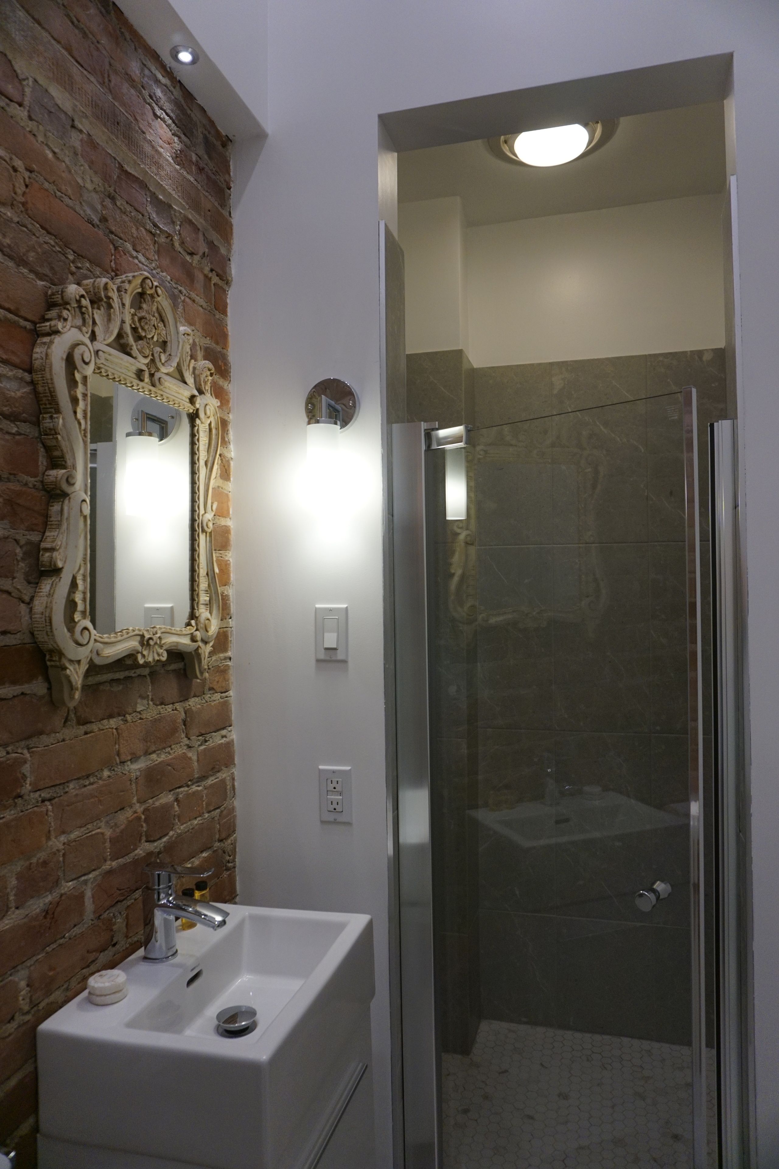 Un baño con un lavabo blanco, un espejo con marco decorativo y una ducha con cerramiento de vidrio.