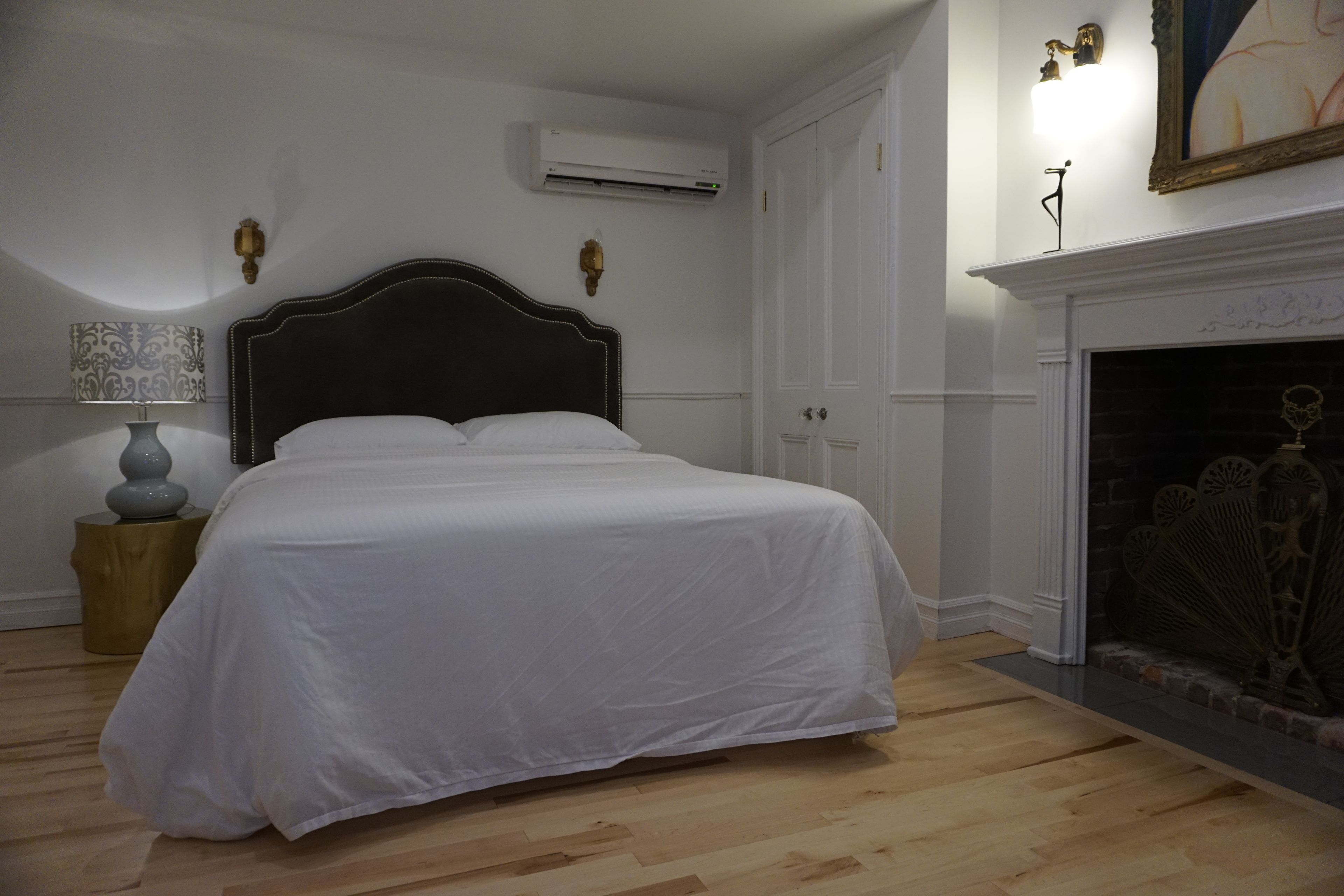 Un dormitorio con una cama grande, una mesita de noche, un equipo de aire acondicionado, una chimenea y una lámpara de pared.