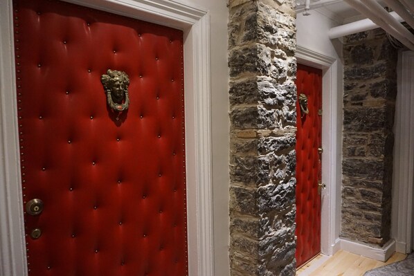 Una puerta roja con un picaporte dorado y una pared de piedra contigua.