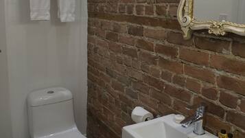 Un baño con inodoro blanco, lavamanos con espejo y toallas colgadas en un perchero.