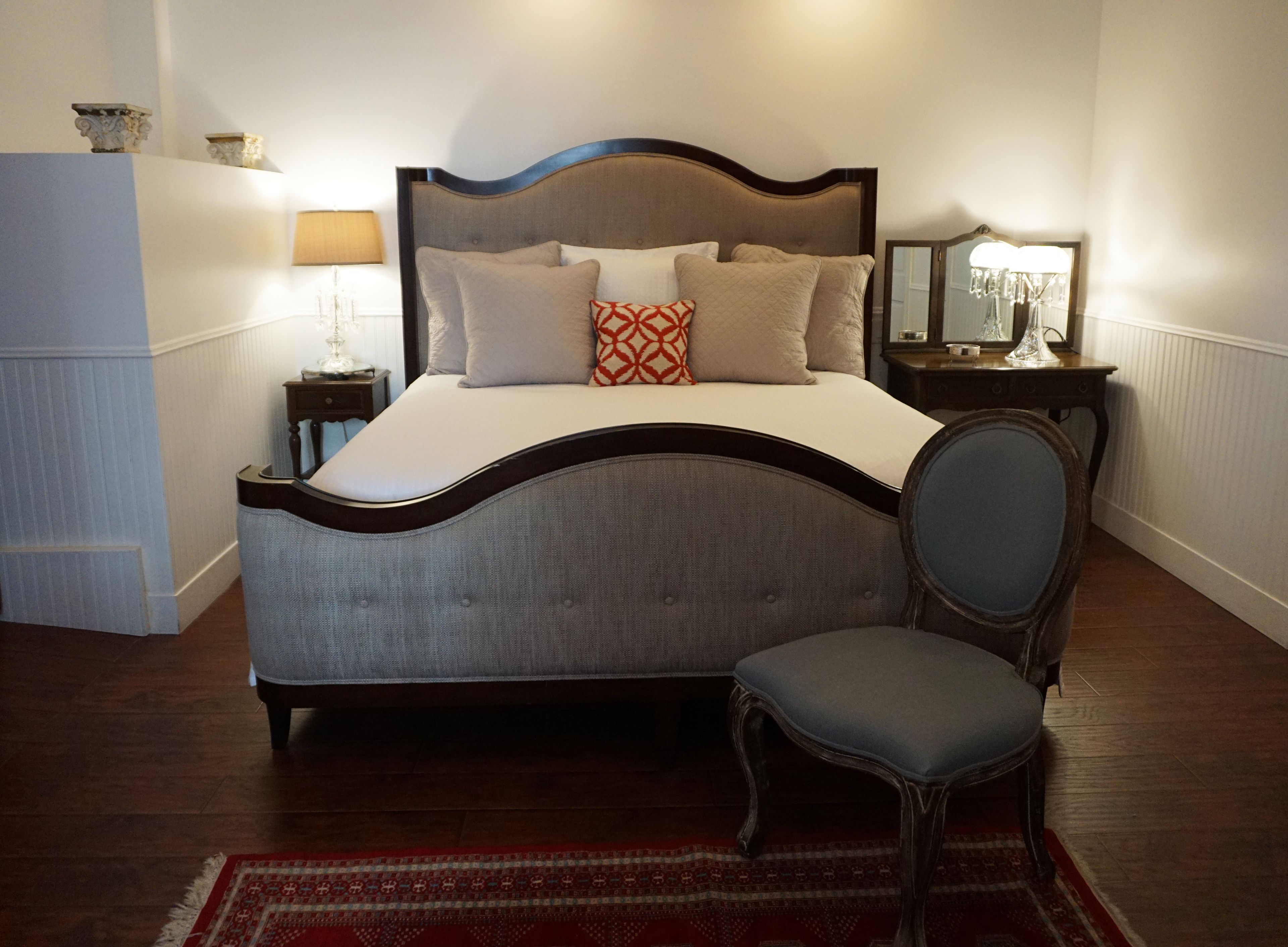 Un dormitorio con cama, una silla, una mesita de noche y una lámpara.