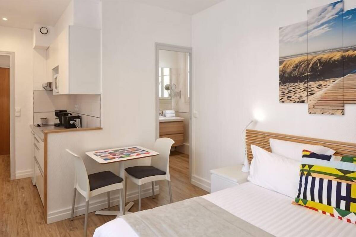 Une chambre comprenant un lit, un bureau avec deux chaises, une petite kitchenette et une salle de bain.