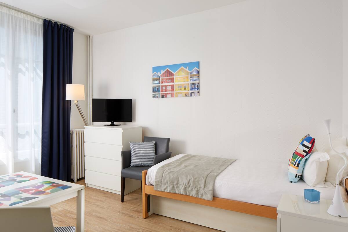 Une chambre d’hôtel bien aménagée, avec un lit, un bureau, une chaise, une télévision et une œuvre d’art murale.