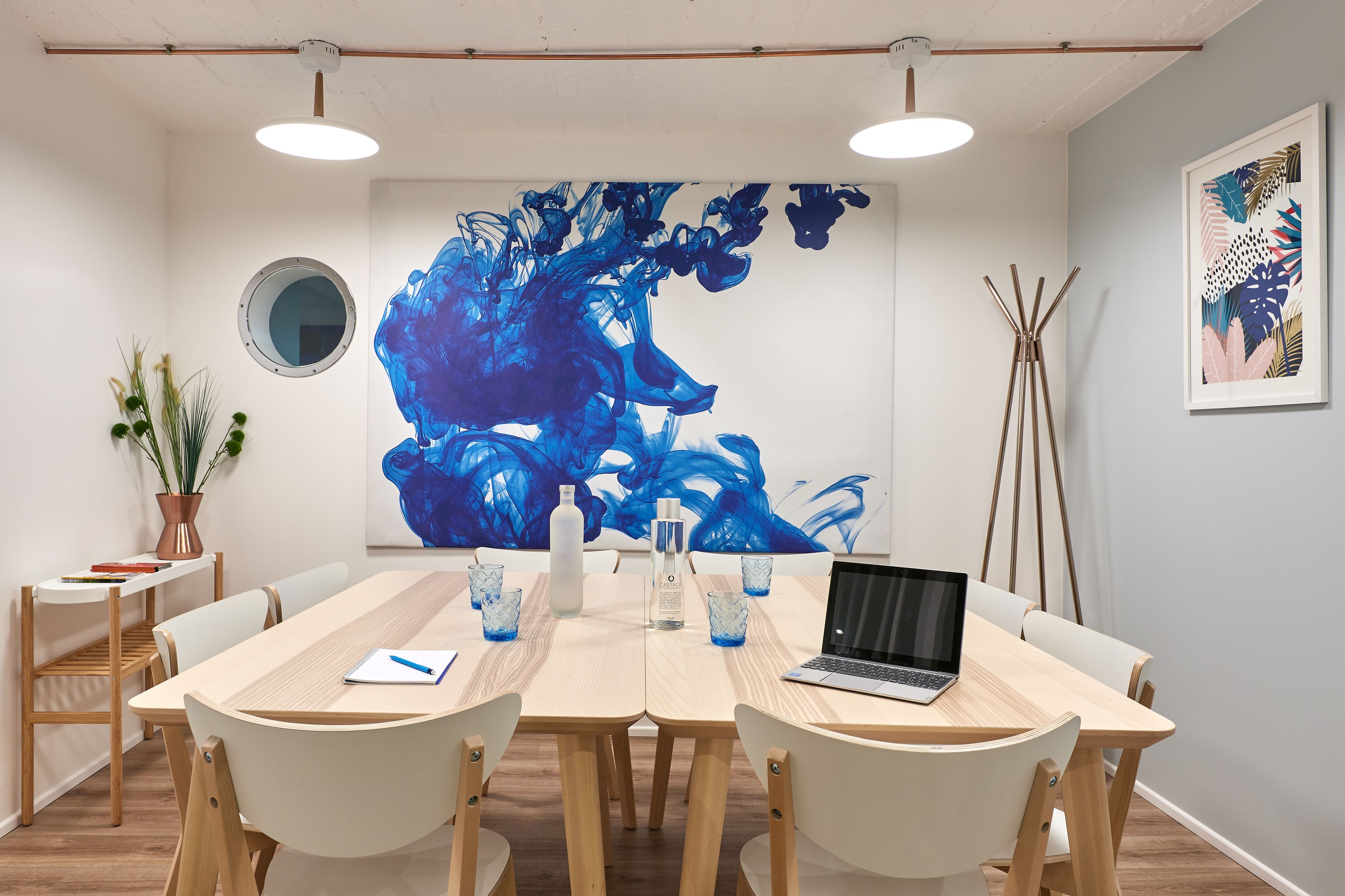 Ein Konferenzraum mit langem Tisch, Stühlen, einem Laptop und einem großen, abstrakten Gemälde an der Wand.