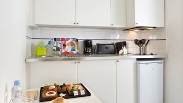 A modern kitchen with white cabinets, a stainless steel countertop, a coffee maker, a toaster, and a small refrigerator.