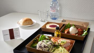 Un plateau contenant divers aliments, notamment du saumon, du riz et une salade, ainsi qu’une bouteille d’eau et un verre.