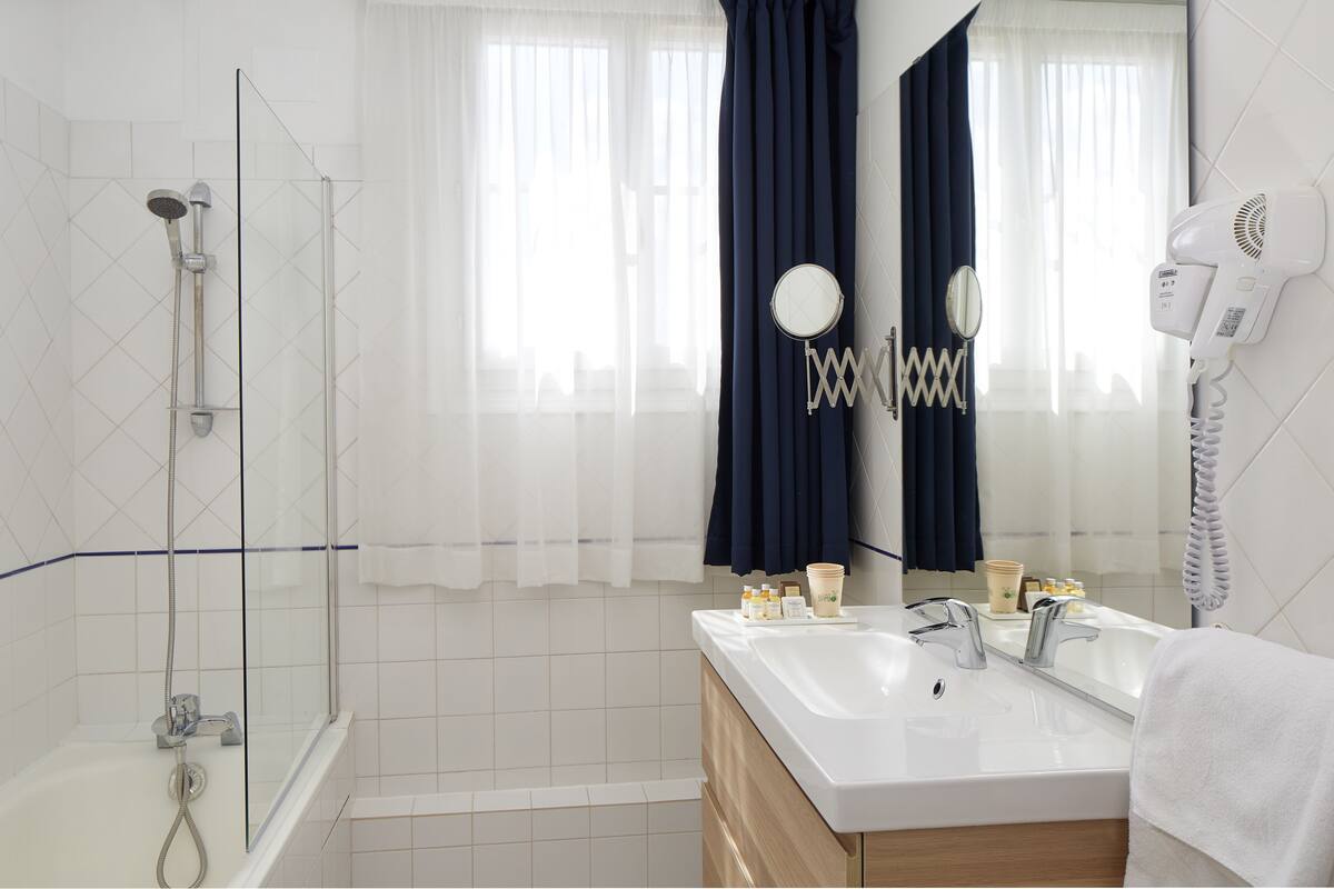 Une salle de bain moderne dotée d’une douche à parois de verre, d’un grand miroir, d’un sèche-cheveux et d’un meuble-lavabo.