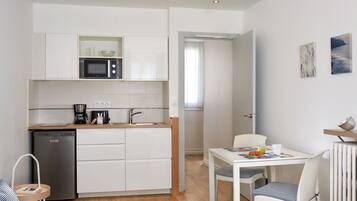 A compact kitchen with white cabinets, a microwave, and a coffee maker. There's a dining area with a table and chairs, and a small refrigerator.