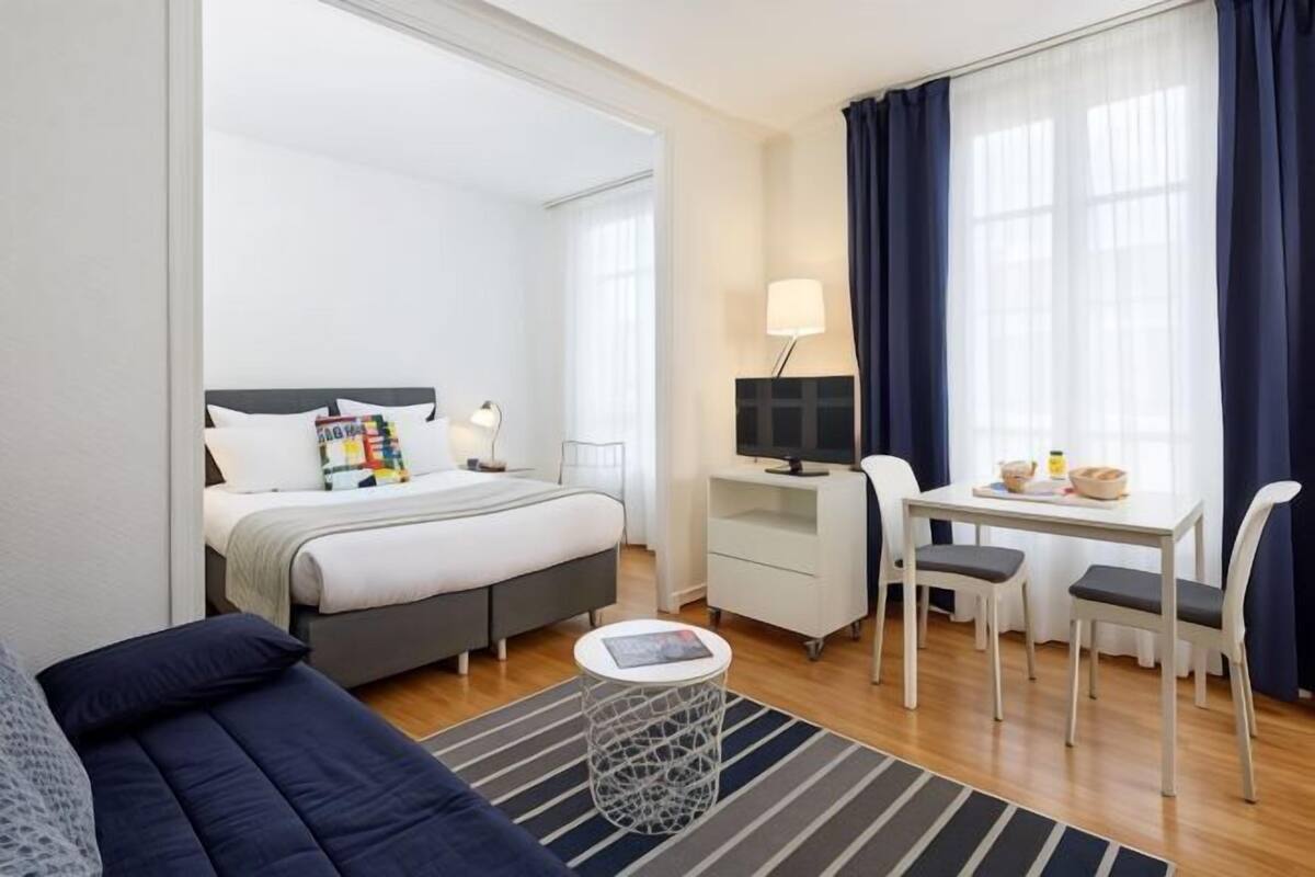 Une chambre d’hôtel moderne équipée d’un lit, d’un bureau avec un ordinateur, d’une chaise, d’une petite table et d’un canapé.