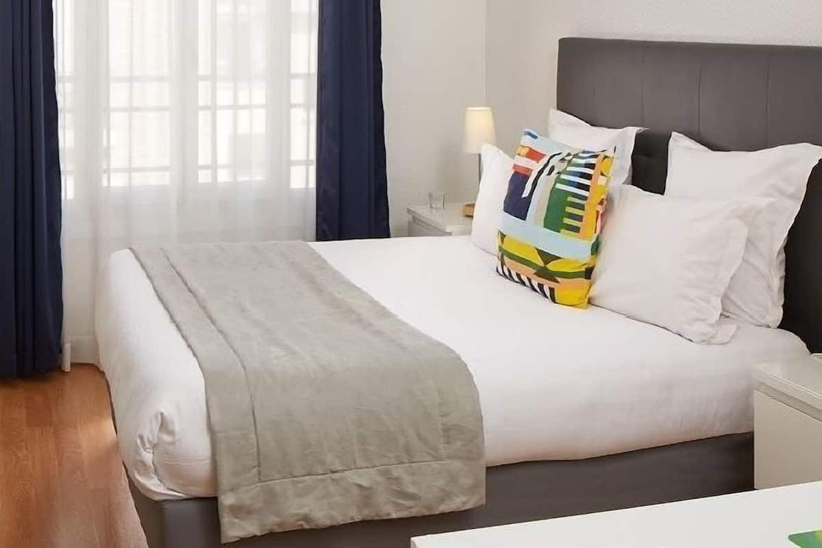 Une chambre d’hôtel avec un lit, une table de chevet avec une lampe et une fenêtre avec des rideaux.