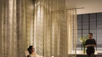 Relax in a serene spa room with a comfortable seating area, window with blinds, and a vase with flowers.