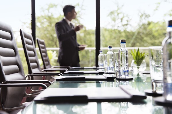 A conference table with chairs, water bottles, and glasses, set in a room with large windows and a view of greenery.