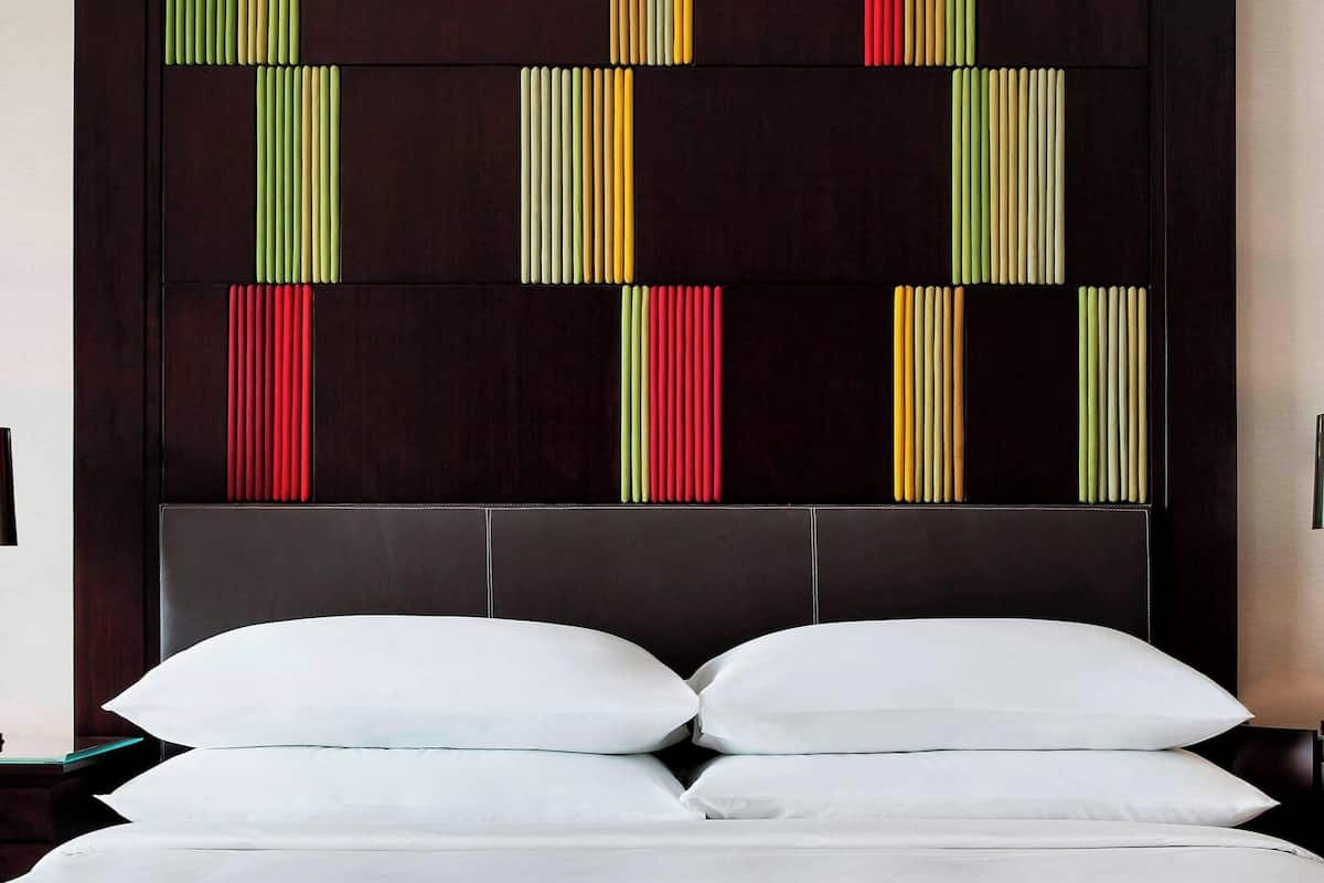 A hotel room with a large bed, a dark headboard with colorful vertical stripes, and white bedding.