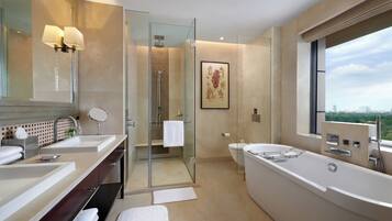 A modern bathroom with two sinks, a large bathtub, a glass-enclosed shower, and a large window offering a city view.