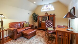 A cozy living room with a brown leather sofa, a matching ottoman, a wooden side table with a lamp, and a wooden chair with a book. - Harvey House Bed & Breakfast (Oak Park)