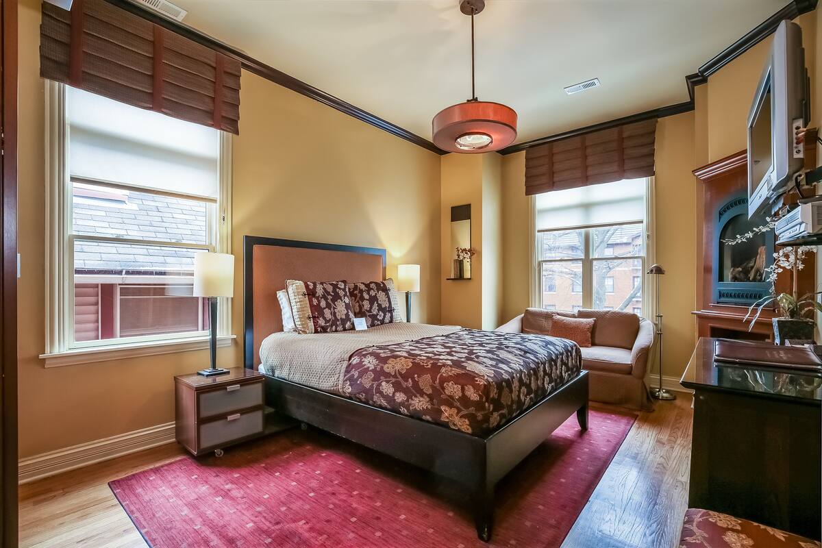 A bedroom with a bed, bedside tables, a desk, a chair, a lamp, and a television.