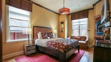 A bedroom with a bed, bedside tables, a desk, a chair, a lamp, and a television.