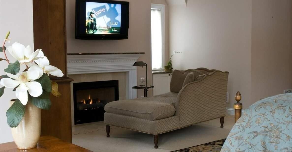 Una sala de estar con un sillón color beige, una chimenea y un televisor montado encima.