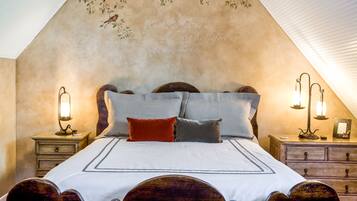 Une chambre à coucher avec un lit en bois, deux tables de chevet avec des lampes et un mur décoratif orné d’oiseaux et de motifs textuels.