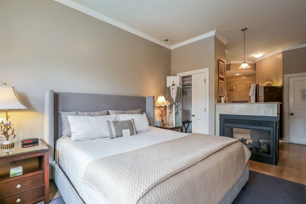 A neatly arranged bedroom with a large bed, bedside lamps, a nightstand, a dresser, and a built-in fireplace.