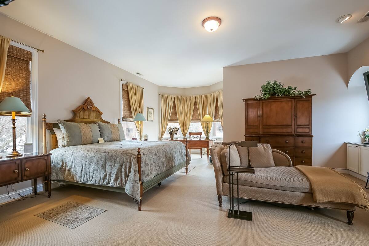 A bedroom with a large bed, a wooden dresser, a chair, and a desk.