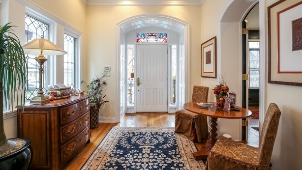 A well-lit hallway with a wooden dresser, a table with chairs, and a blue patterned rug. - Harvey House Bed & Breakfast (Oak Park)