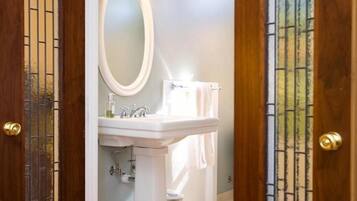 Un baño con lavamanos blanco, espejo y toallero.