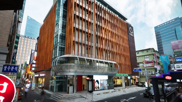 A modern hotel with a distinctive wooden facade, a glass entrance, and an overhanging structure. - Metro Hotel (Seoul)