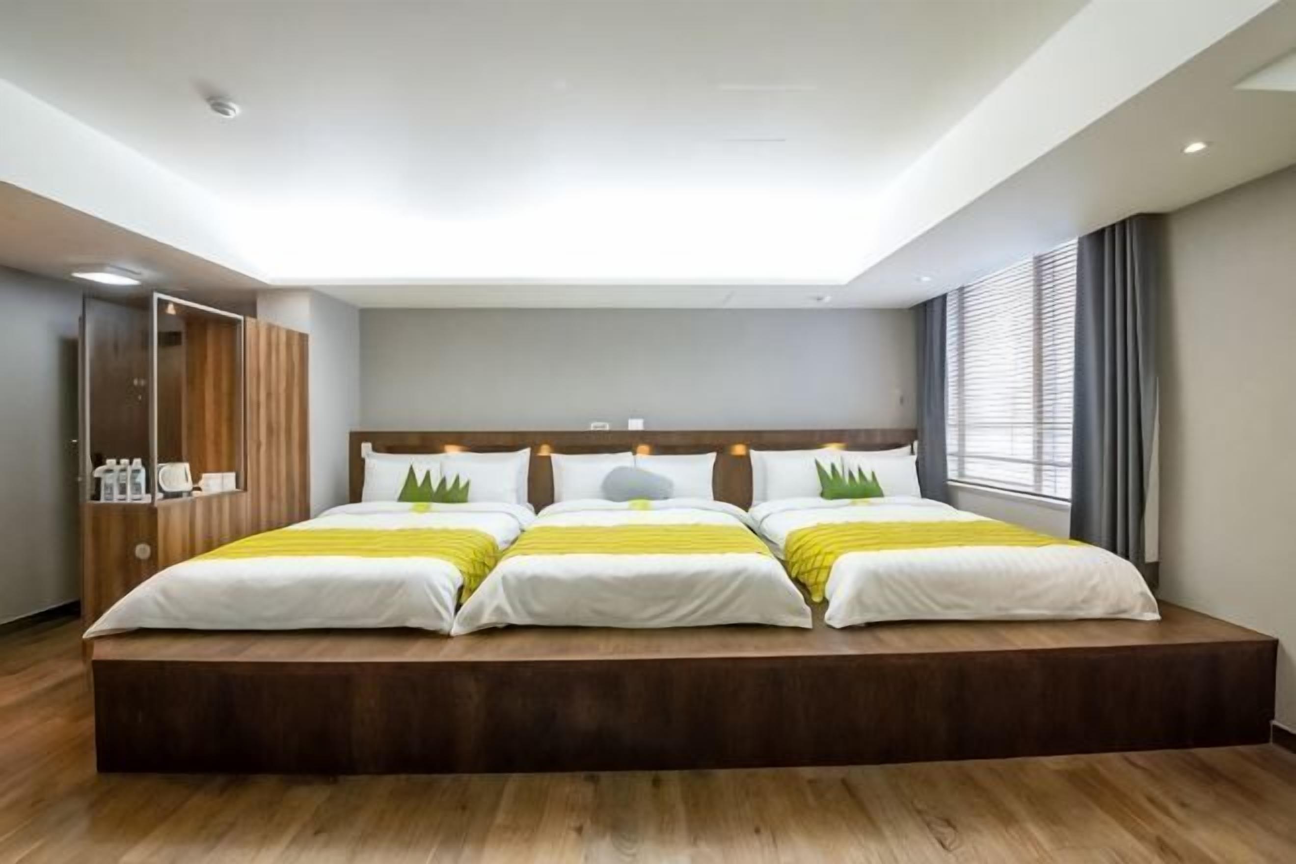 A large bed with a wooden platform, a mirror, and a window with curtains.