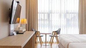 A hotel room with a bed, a desk with a lamp, a chair, and a TV.