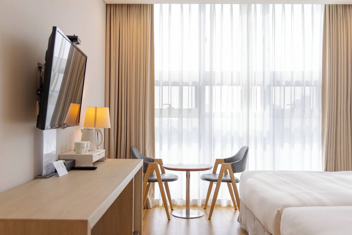 Ein Hotelzimmer mit Bett, Schreibtisch mit Lampe, Stuhl und Fernseher.