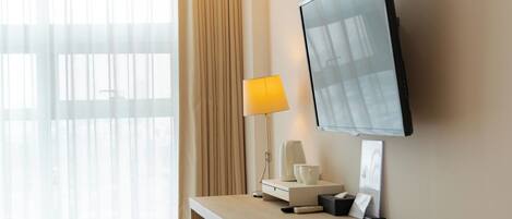 Habitación de hotel con televisor de pantalla plana montado en la pared, una mesita de noche con lámpara, cafetera y control remoto.