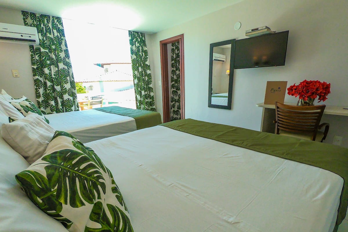 A hotel room with two beds, a desk with a chair, a mirror, and a vase with red flowers.