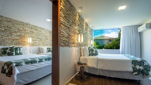 A hotel room with two beds, a stone wall, a small table, and a window with a view of greenery. - Hotel Experience João Fernandes (Búzios)