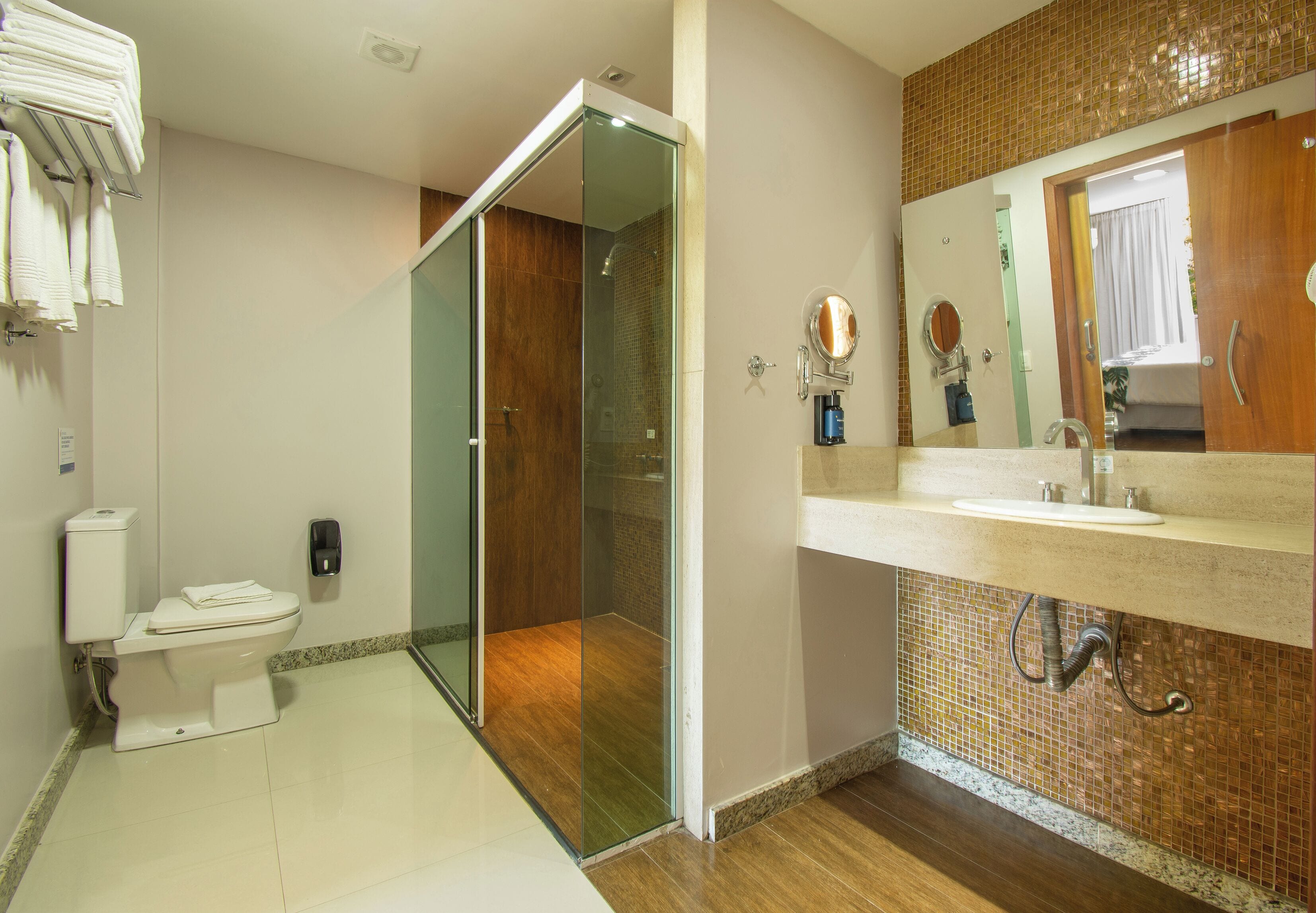 Une salle de bain moderne avec une douche à parois de verre, des toilettes, un lavabo avec un miroir et un porte-serviettes.