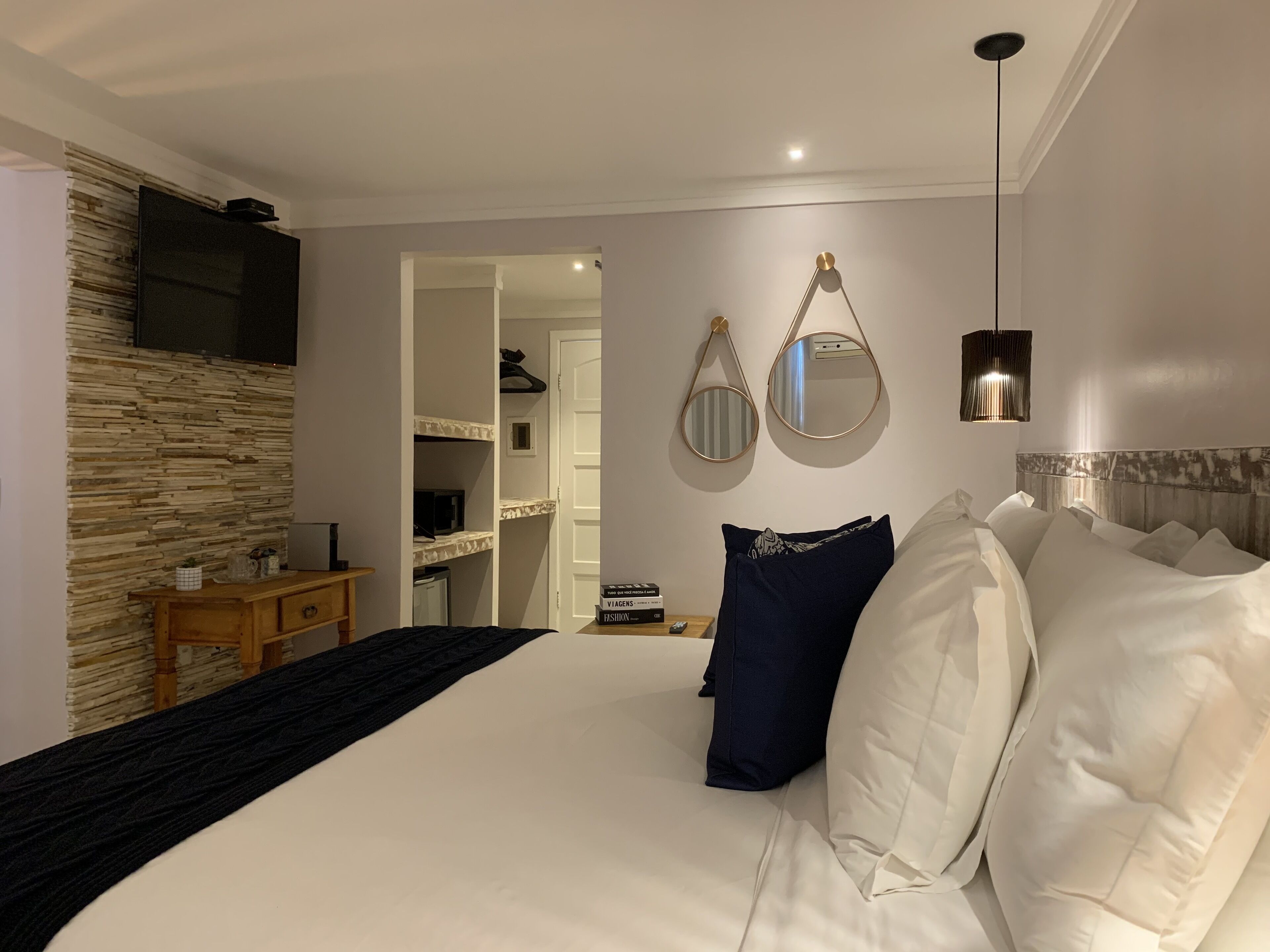 Una habitación de hotel moderna con una cama grande, un aparador de madera, un televisor montado en la pared y un espejo sobre el aparador.