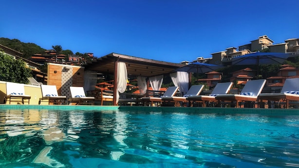 A clear swimming pool with lounge chairs and a covered seating area. - Hotel Experience João Fernandes (Búzios)