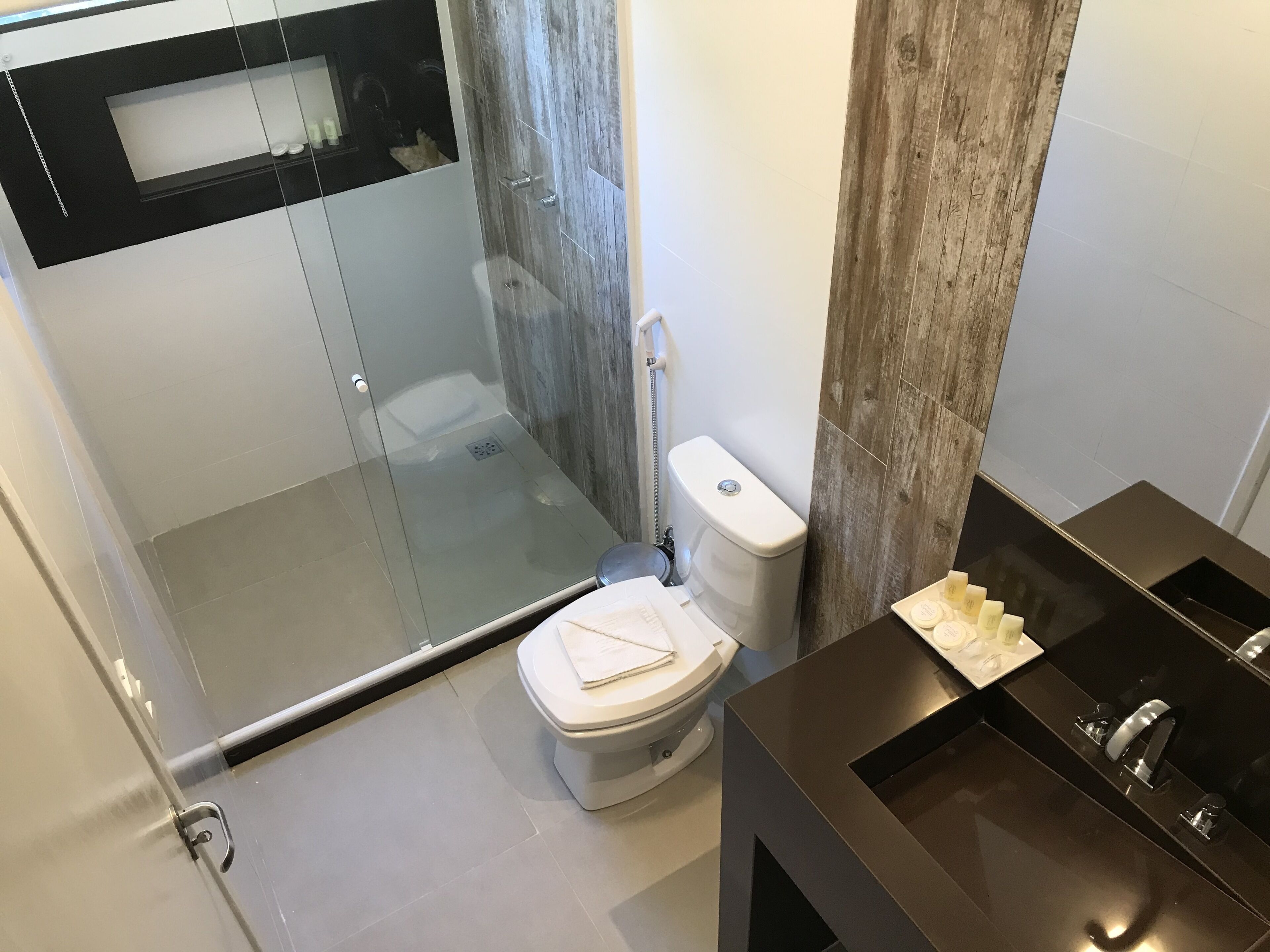 Un baño moderno con cabina de ducha de vidrio, un inodoro y un lavabo sobre un mueble negro.